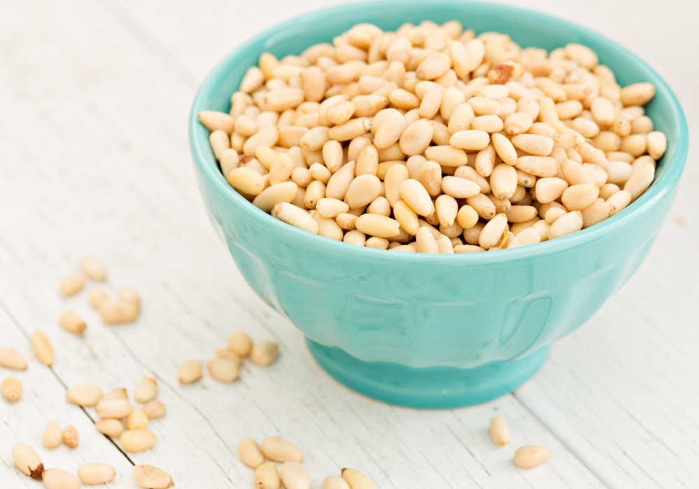 This image shows a blue bowl filled with pine nuts, which is the key ingredient to make pine nut parmesan, an easy plant-based alternative.