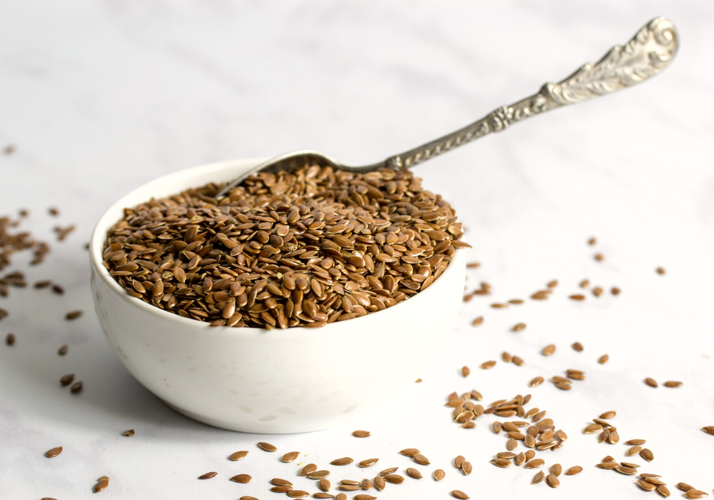 This image shows a white bowl overflowing with whole flax seeds, which are the key ingredient to make the plant-based alternative flax eggs.