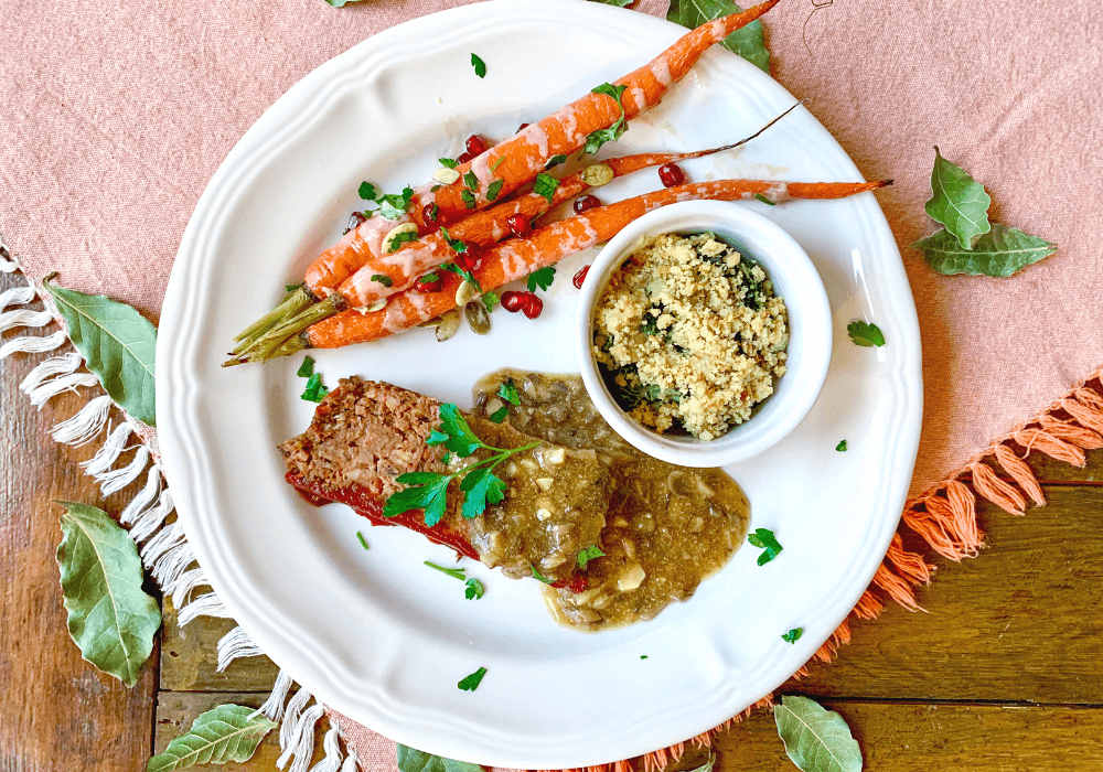 This image shows a completely plant-based meal that is very similar to a standard American dinner. It has plant-based meatloaf, mushroom gravy, roasted carrots, and a creamy kale gratin. 