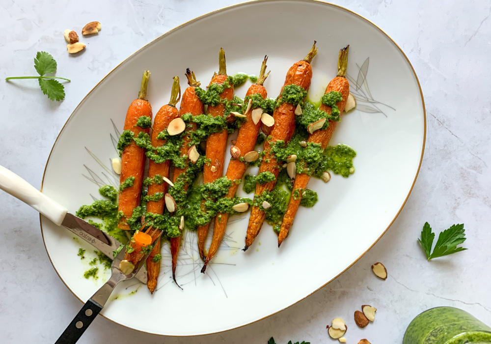 This image shows the maple-roasted carrots with chimichurri sauce drizzled over them and sprinkled with toasted almonds.