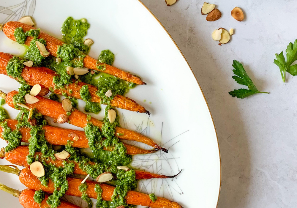 This image shows the maple-roasted carrots with chimichurri sauce drizzled over them and sprinkled with toasted almonds.