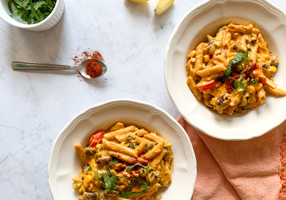 Healthy loaded mac & cheese served in bowls with extra smoked paprika, lime, and coriander on the side.