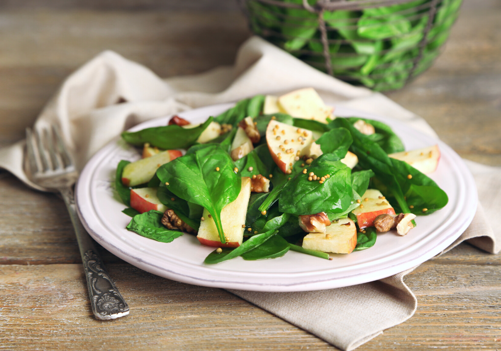 This image shows the perfect starter for a plant-based Valentine's dinner: a leafy green salad with sliced apples and nuts.