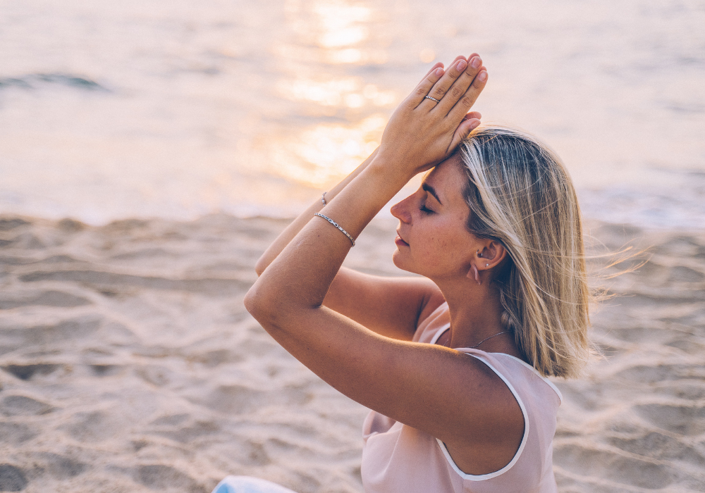 This image shows a woman doing yoga on a beach at sunrise. She looks peaceful without any stress.