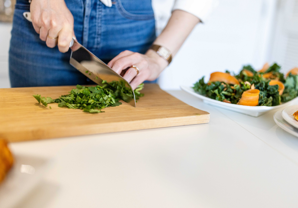 This image shows a woman chopping herbs on a cutting board with a sharp knife.