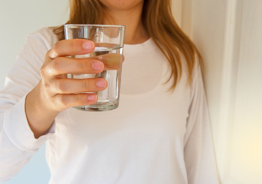 The first of the holistic habits for a plant-based diet is to hydrate. Image of woman holding a glass of water.