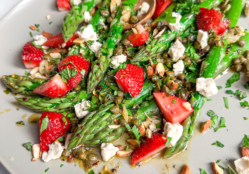 This image shows a closeup of a strawberry asparagus salad on a light grey platter.