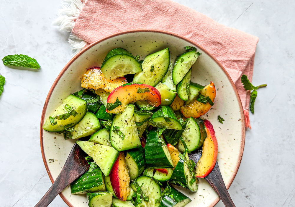 This image shows a close up of the cucumber and peach salad in a cream colored bowl with an orange napkin.