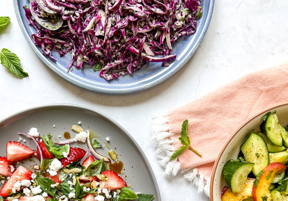 This image shows a close up of three quick and easy summer salads on platters on a light background with an orange napkin.