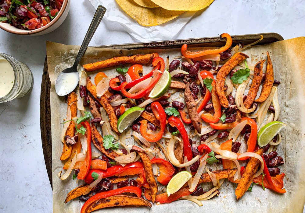 This image shows an example meal of what one might eat to thrive on a plant-based diet. It shows a baking pan with roasted veggies, corn tortillas, and a white sauce on a spoon.