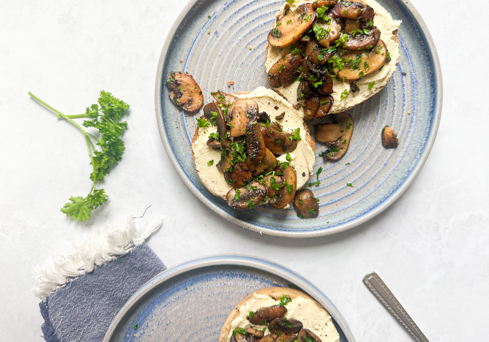 This image shows a two blue plates on a white surface with two slices of bread and the Dairy-Free Ricotta & Sauteed Mushrooms on top.