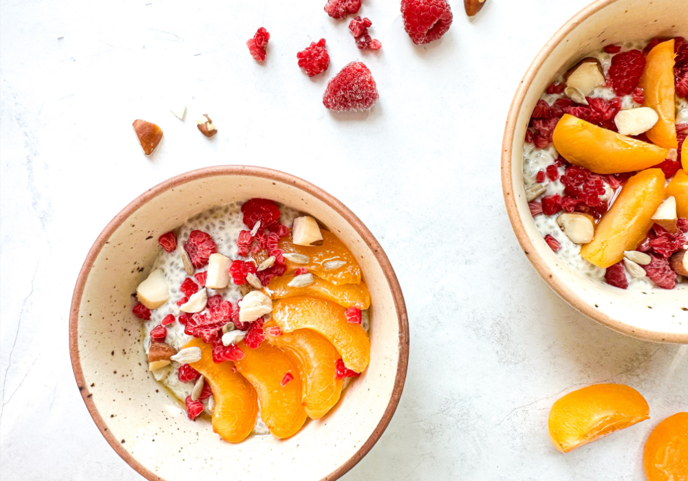 This image shows two creamy chia yogurt bowl on a white surface filled with fresh fruit and nuts.
