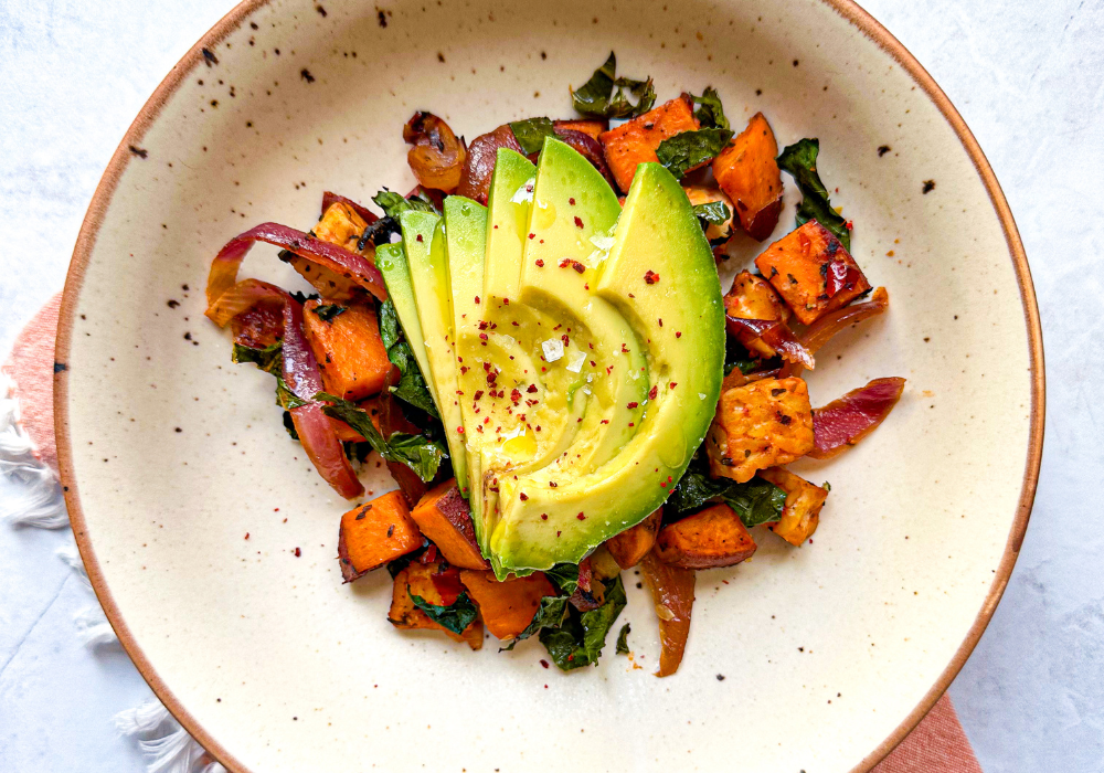 This image shows a plant-based hash in a cream bowl with sliced avocado on top, part of the plant-based breakfast recipes series.