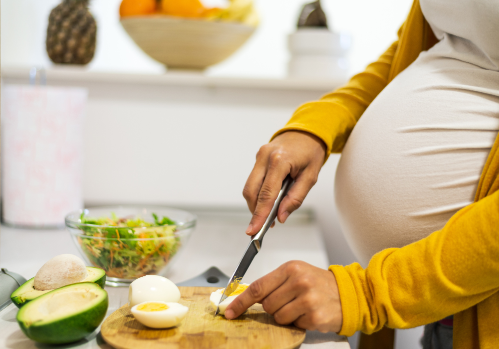 This image shows a close-up of a pregnant woman cutting an egg to put in a salad with avocado--two key foods to eat for a healthy pregnancy.