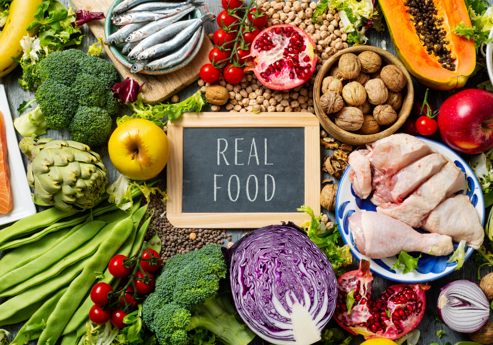 This image shows a variety of different foods to eat for a healthy pregnancy arranged on a flat surface with the words "Real Food" on a chalkboard in the center.